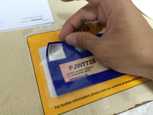 Applying the Malaysia Road Tax Sticker with transparent plastic on the etiQa car decal